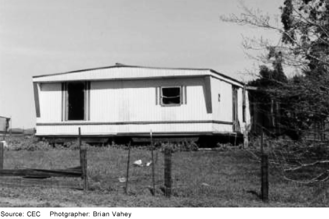 A manufactured or mobile home on a lot with grass and a fence